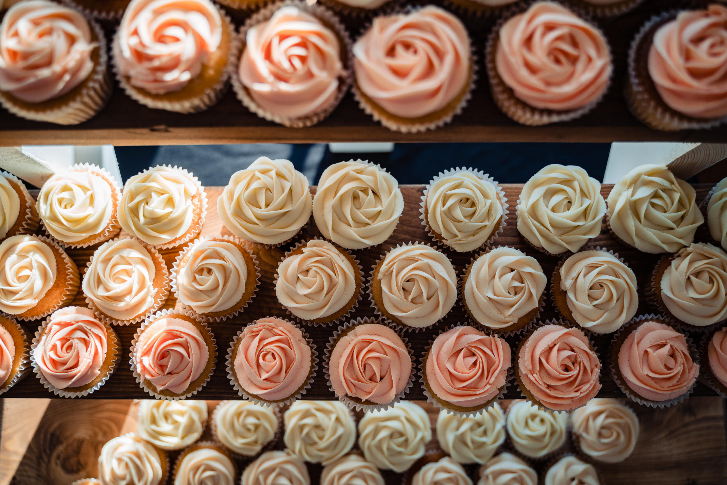 A bunch of pink and cream cupcakes sit on a stand