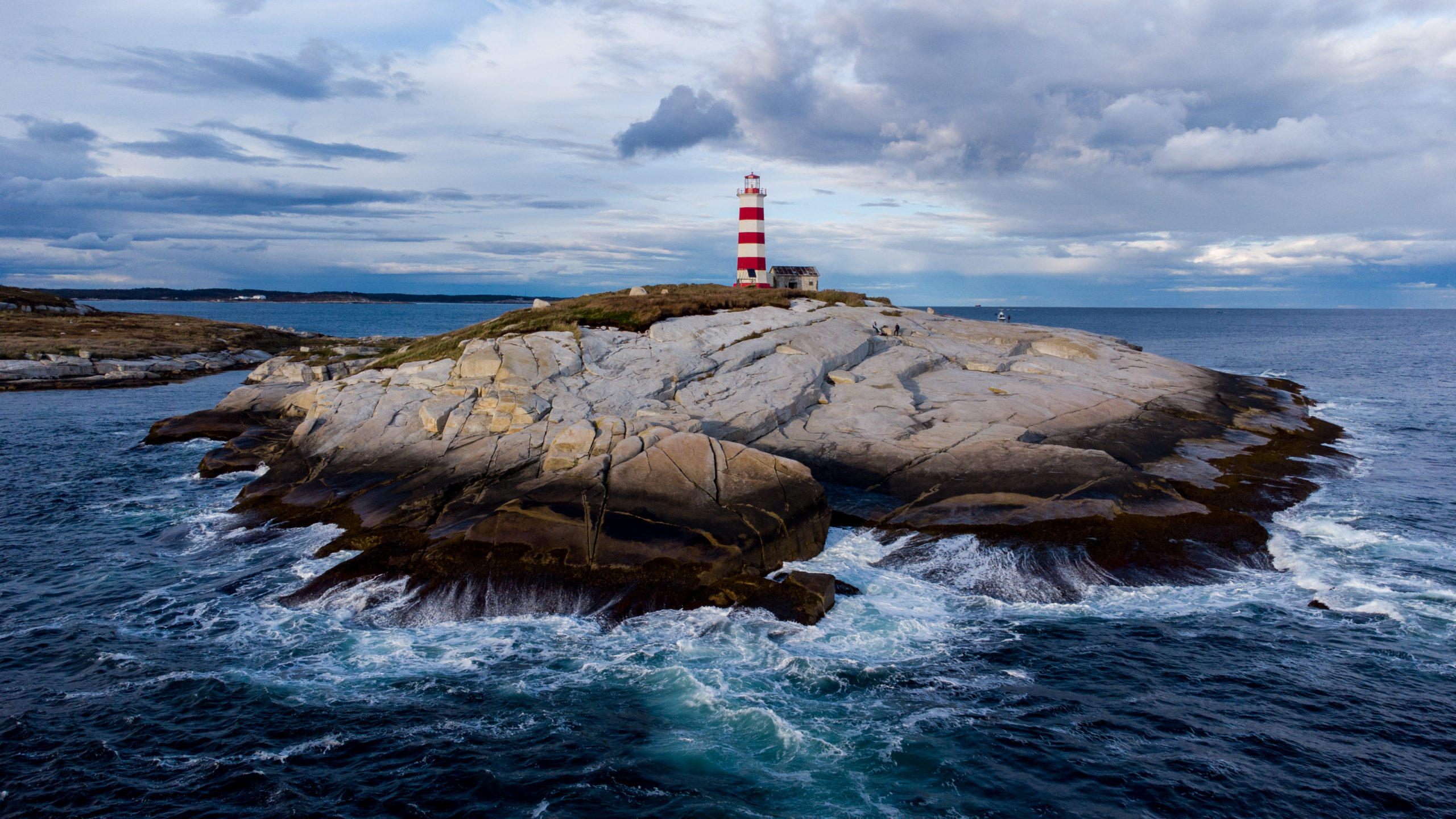 A rocky rugged landscape of an island with a white and red lighthouse and ocean waves splashing on the rock